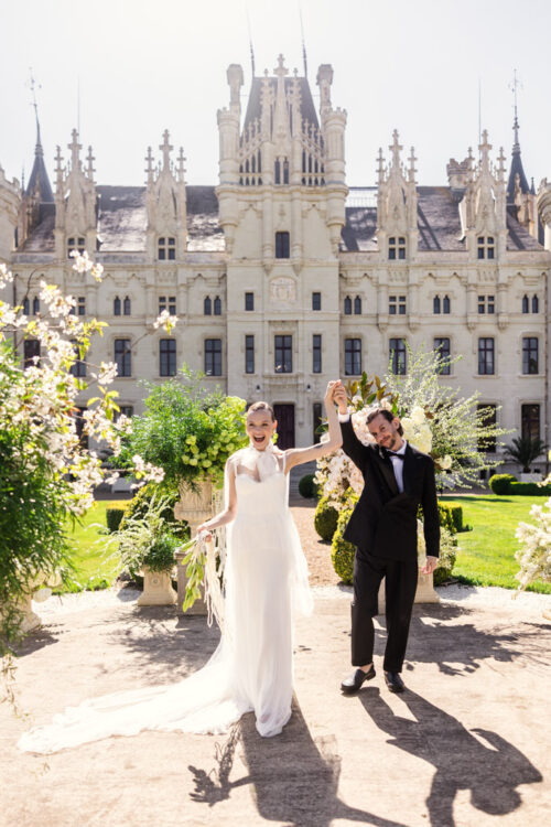 Bride and groom celebrate outside Chateau Challain, holding hands and smiling in the sunlight on their wedding day
