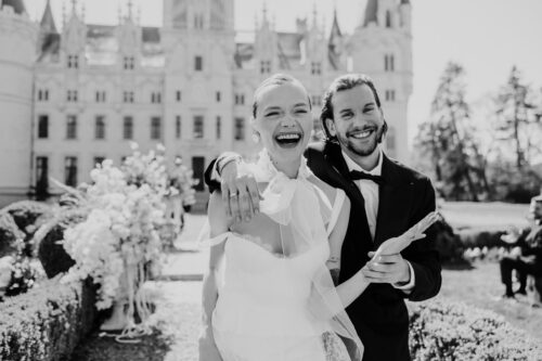 Black and white photo of bride and groom smiling outside Chateau Challain on their wedding day
