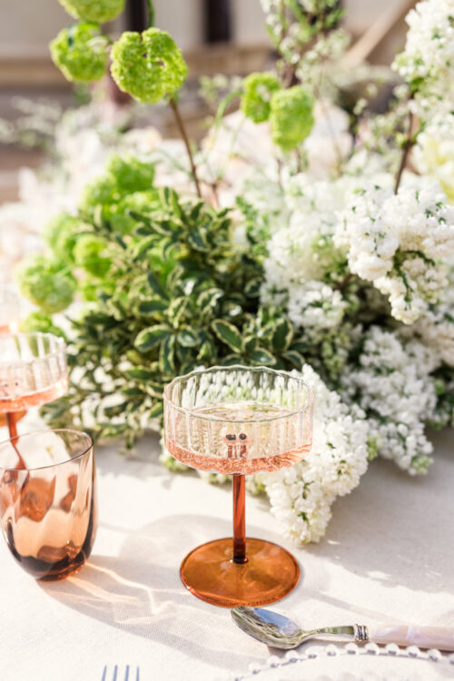 Glass of sparkling wine on a table with a lush green and white floral centerpiece in sunlight for Chateau Challain outdoor wedding reception