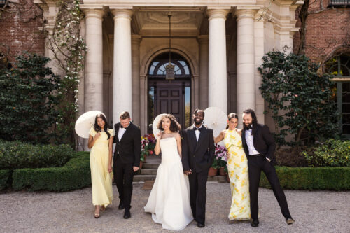 Wedding party in formal attire stands smiling outside the grand columns of a building at Filoli Historic House & Gardens