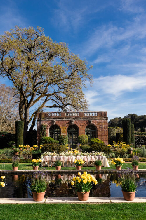 Guest table for wedding reception with brick building with arched windows in the background and a reflecting pool for wedding reception at Filoli Historic House & Gardens