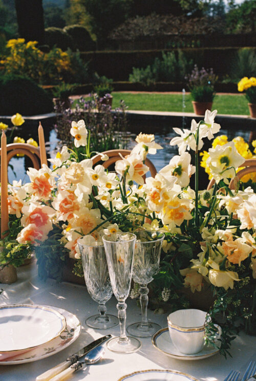 Elegant outdoor wedding table setting with glassware and a yellow-white floral arrangement beside a pond at Filoli Historic House & Gardens