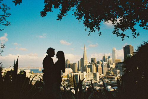 Film photo silhouette of engaged couple with the iconic San Francisco skyline in the background under a clear, blue sky