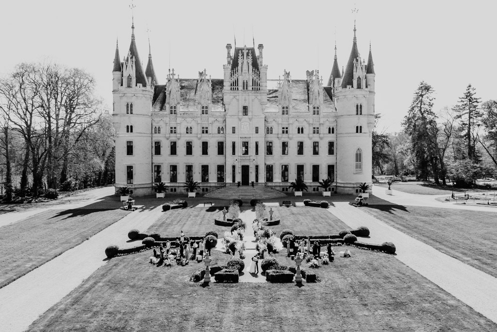 A grand French castle wedding venue with towers and formal gardens, viewed from the front in black and white.