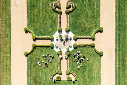 Aerial view of a symmetrical garden at a French castle wedding, with guests gathered on the grass, possibly for an outdoor event.