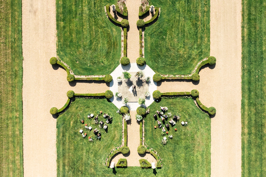 Aerial view of a symmetrical garden at a French castle wedding, with guests gathered on the grass, possibly for an outdoor event.