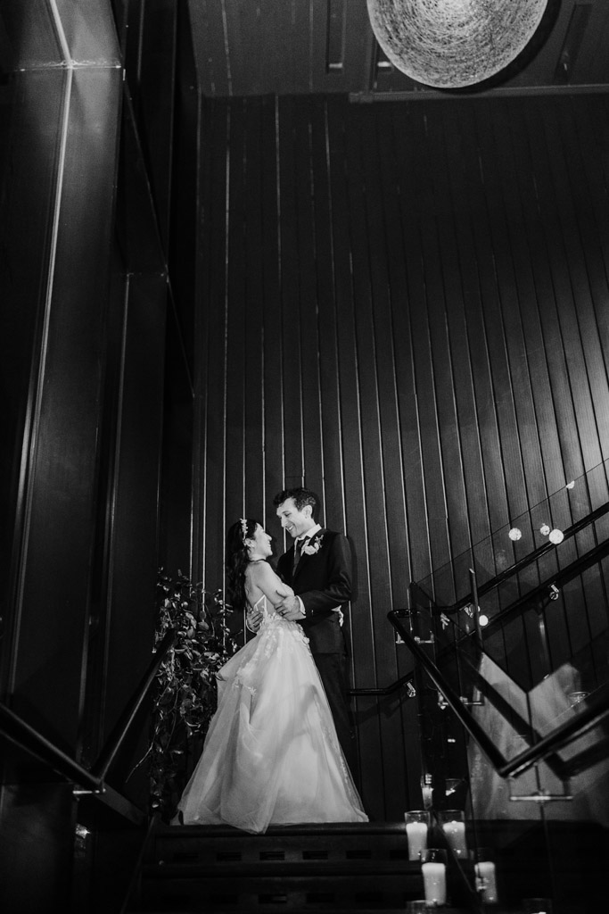 Bride and groom smile at each other while standing together on a staircase at Chicago Winery, surrounded by the warm glow of candles
