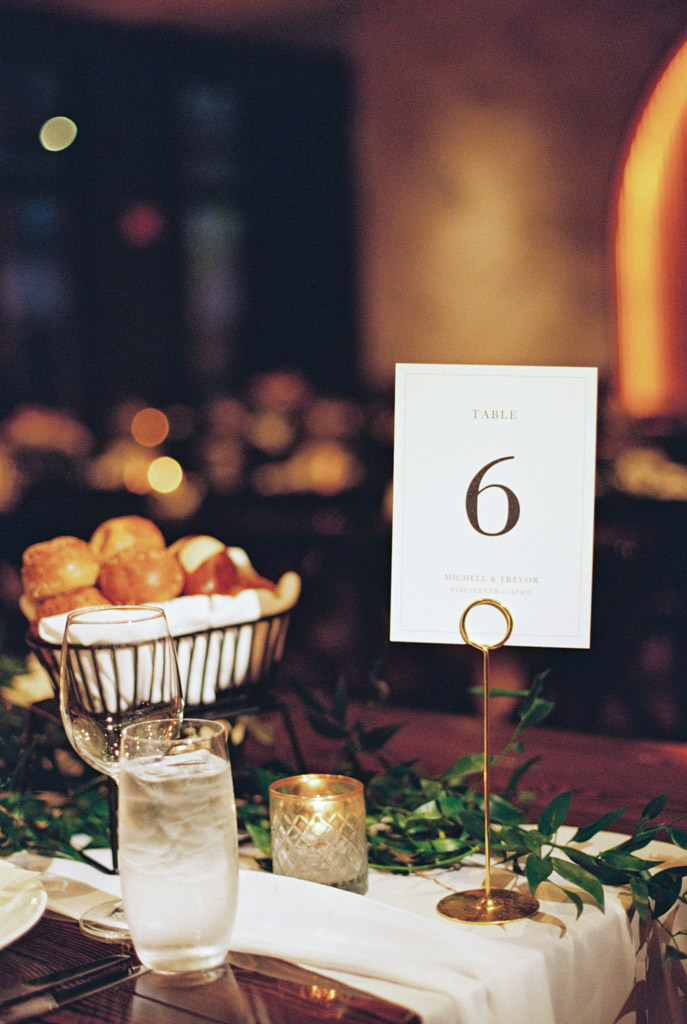 Guest table sign with glass of water, bread basket, candle, and greenery centerpiece for Chicago Winery wedding reception