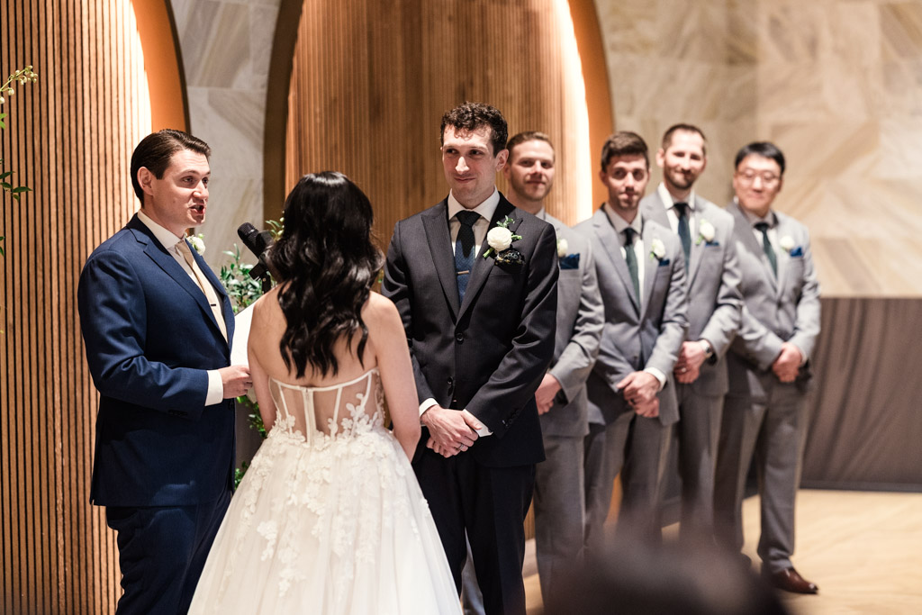 Bride and groom stand with officiant and groomsmen in suits during a wedding ceremony at Chicago Winery