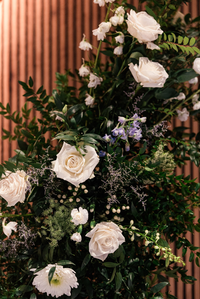 A floral arrangement with white roses and greenery set against vertical wooden slats for Chicago Winery wedding celebration