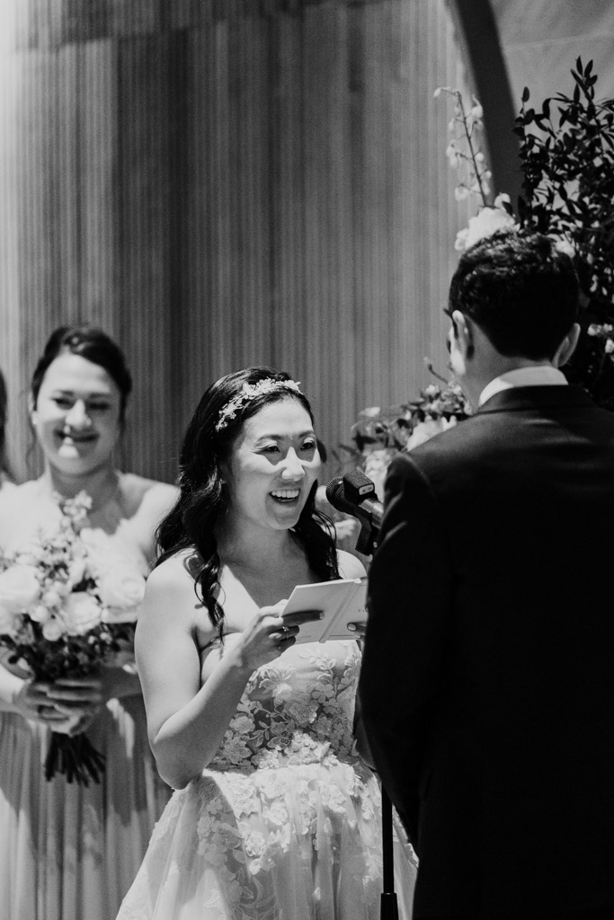 Black and white photo of bride smiling while reading vows to her groom at Chicago Winery