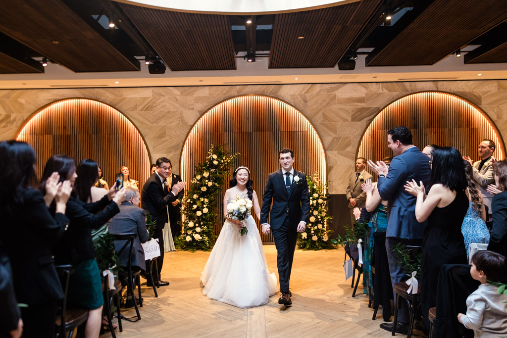 Newlyweds walk down the aisle, smiling, as guests applaud during their Chicago Winery wedding ceremony