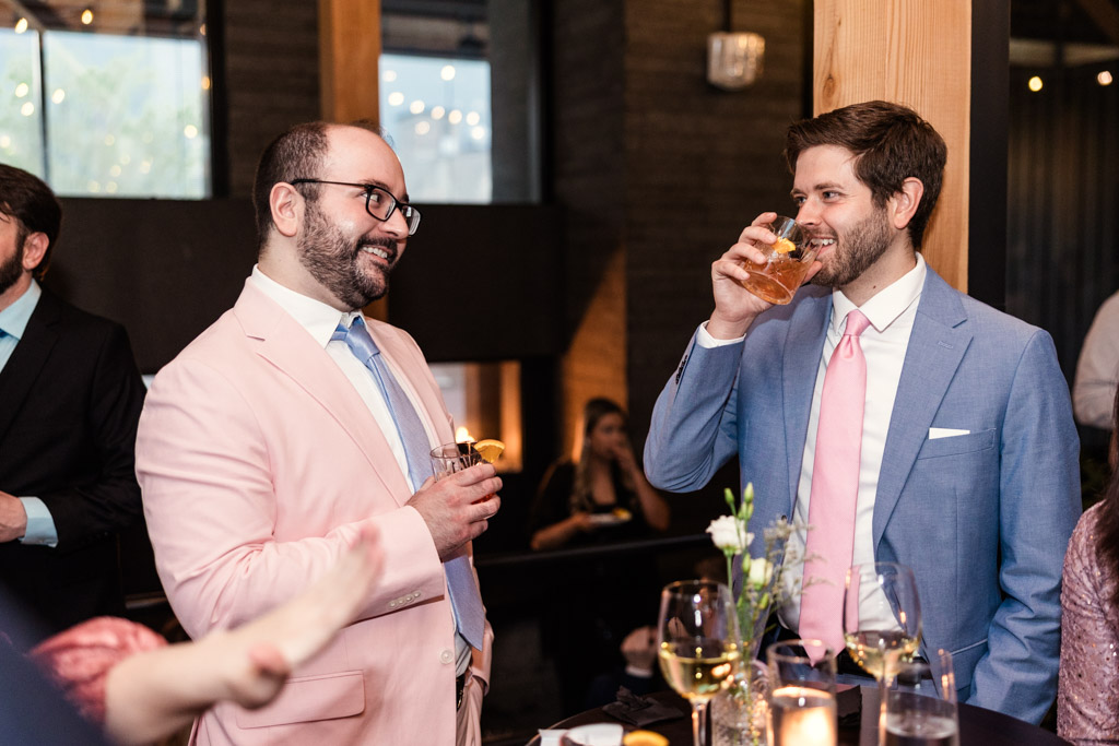 Two guests in suits smile and drink cocktails at Chicago Winery wedding reception