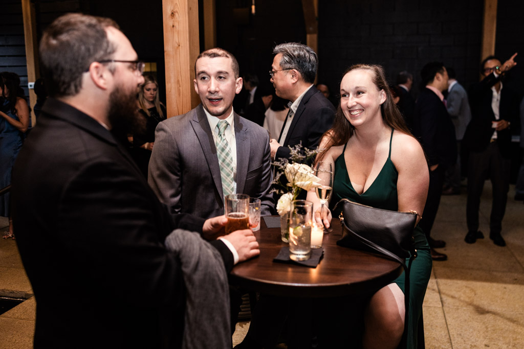 Three guests in formal attire chat and smile around a small table with drinks at Chicago Winery wedding reception