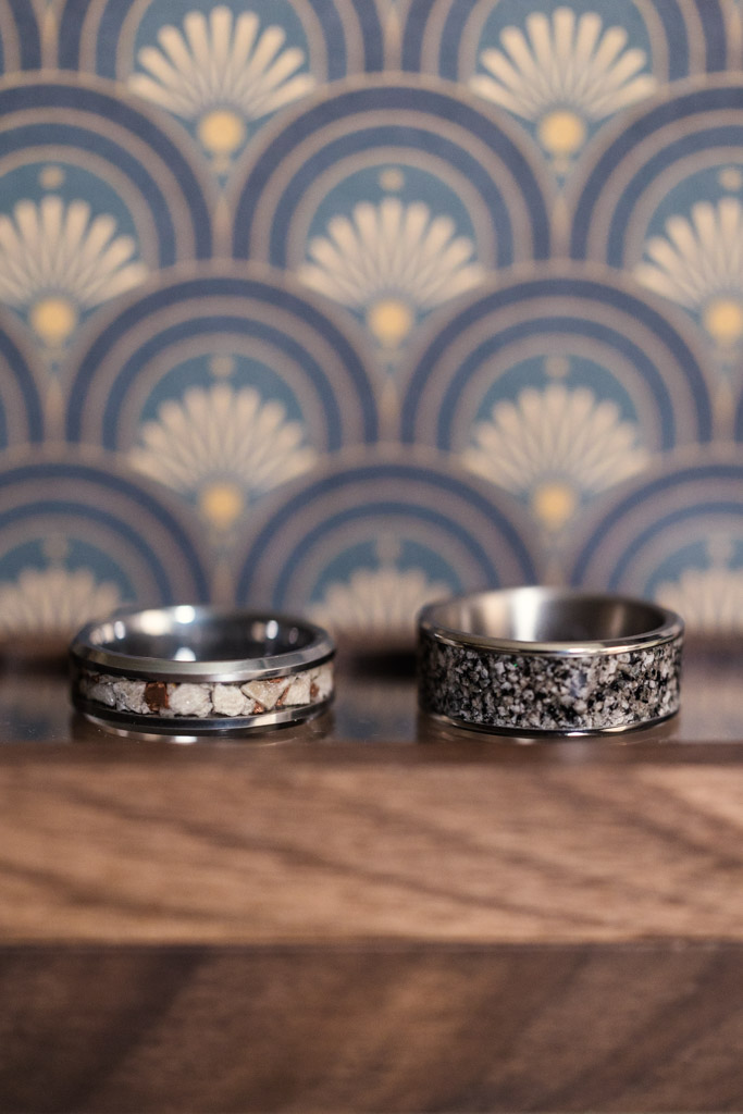 Two patterned rings rest on a wooden surface, set against a blue and gold art deco backdrop for Chicago Winery wedding celebration