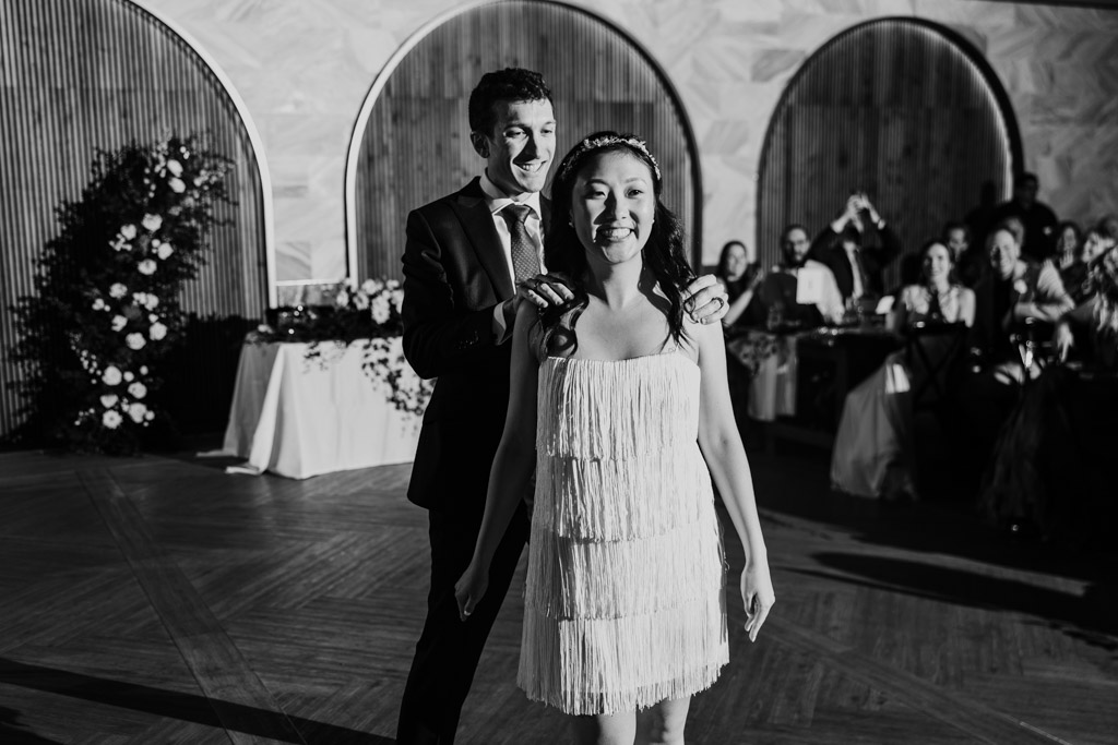 Black and white photo of happy newlywed couple dancing together at their Chicago Winery wedding reception, watched by seated guests in the background