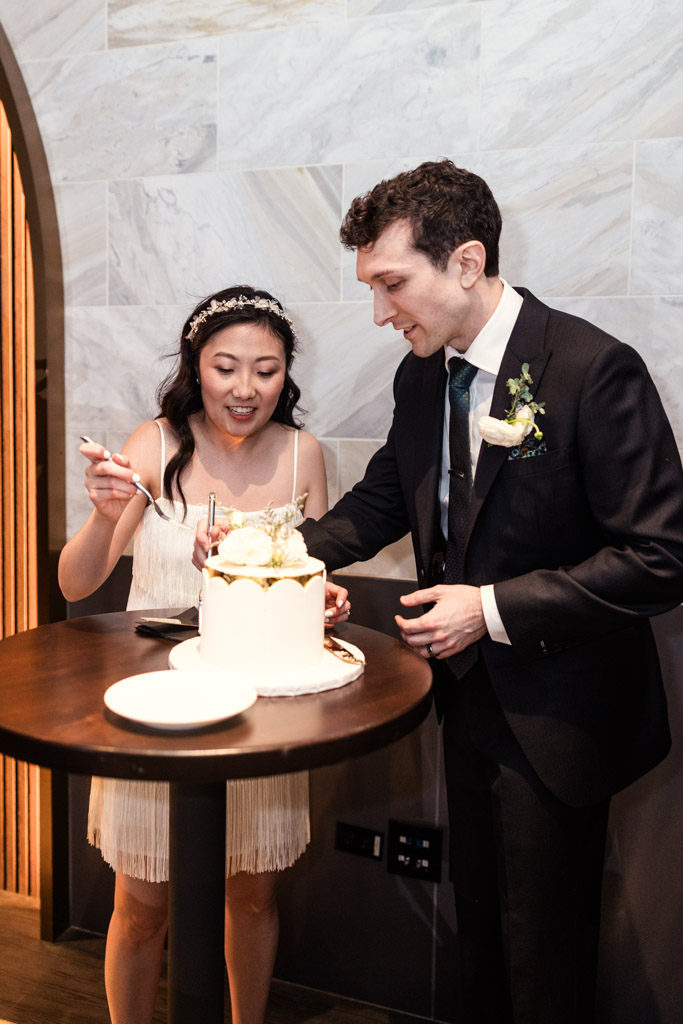 Bride and groom prepare to eat their wedding cake together at a small round table during their Chicago Winery wedding reception