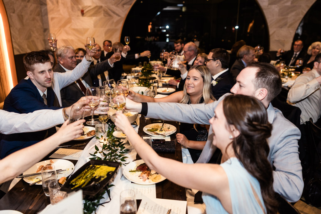 Guests raising glasses for a toast, seated around a long decorated table at Chicago Winery wedding reception