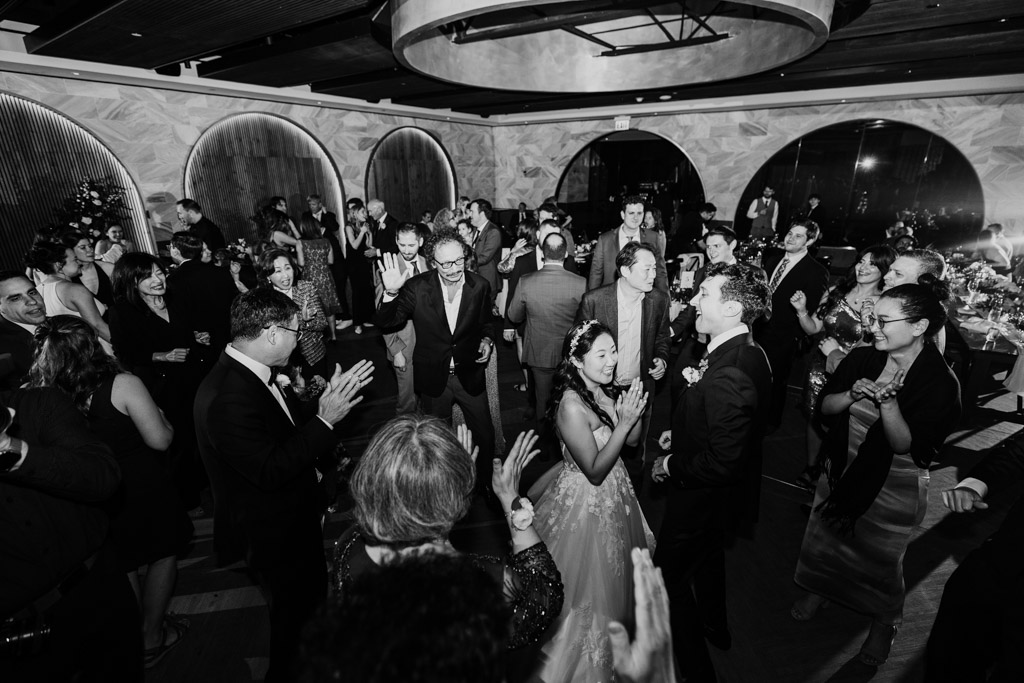 Black and white photo of wedding guests dancing around the bride and groom inside Chicago Winery reception space