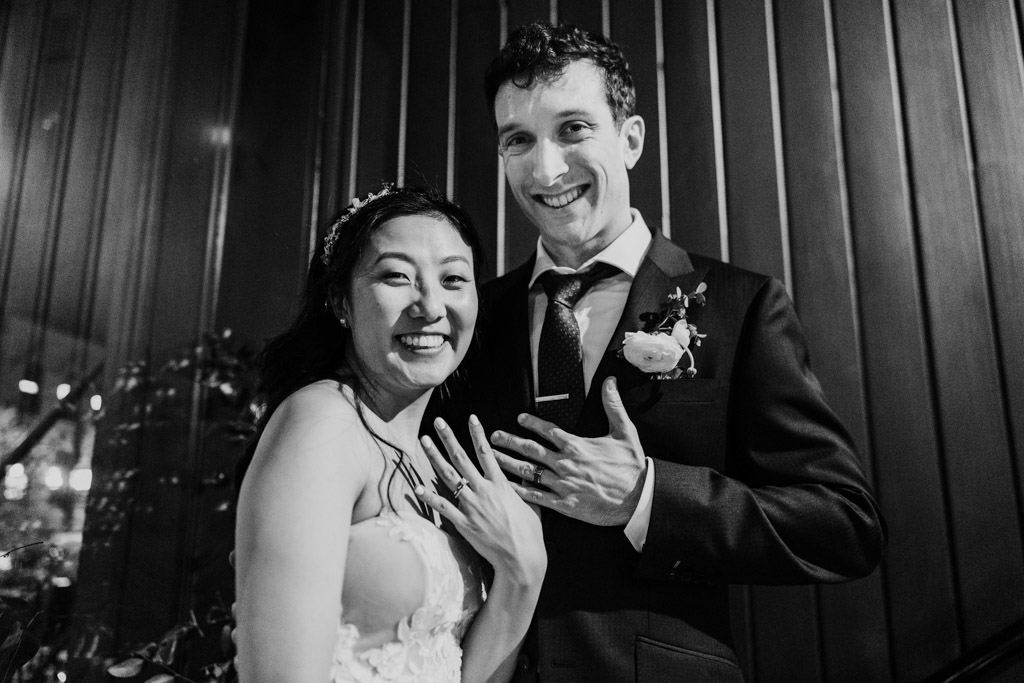 Black and white photo of smiling newlywed couple showing off their wedding rings at Chicago Winery