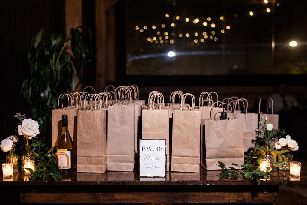 Guest favors table for Chicago Winery wedding reception displays brown paper gift bags, candles, flowers, and custom sign