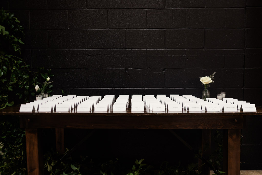 Wooden table with rows of white place cards, set against a black brick wall at Chicago Winery