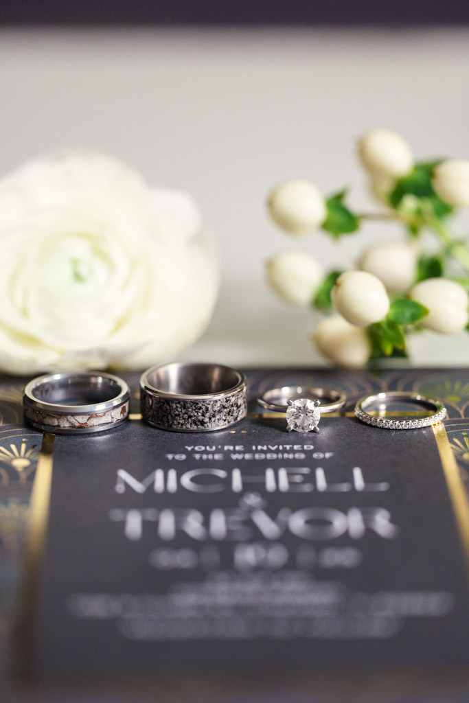 Detail photo of four rings on a wedding invitation, with white flowers and berries in the background