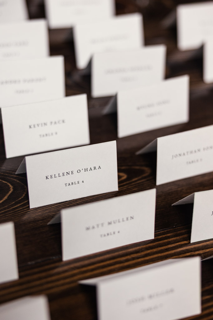 Rows of white place cards with guest names and table numbers arranged on a dark wooden surface for Chicago Winery wedding reception