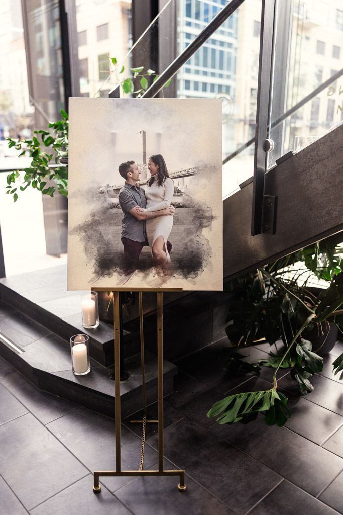 Newlywed couple’s portrait on an easel, displayed indoors near stairs at Chicago Winery, with green plants and candles nearby