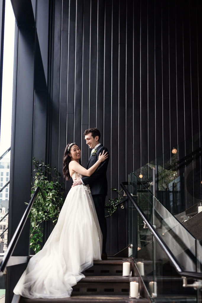 Bride and groom hold each other on a modern indoor staircase at Chicago Winery, beautifully decorated with greenery and candles