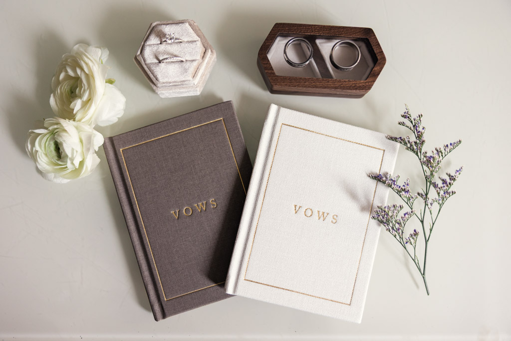 Two vow books, wedding rings in boxes, and white flowers arranged on a white surface for Chicago Winery wedding celebration