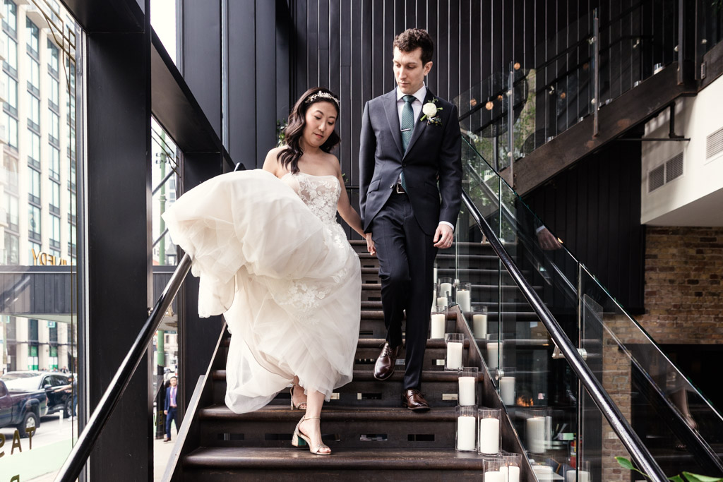 Bride and groom walking down a modern staircase at Chicago Winery, holding hands, with candles lining the steps