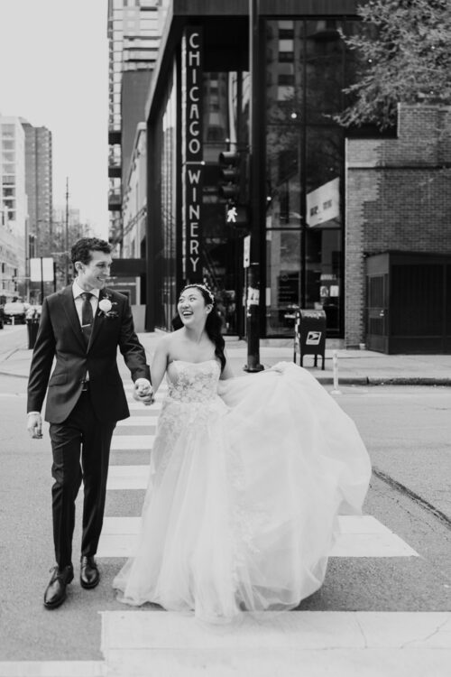 Black and white photo of bride and groom holding hands as they cross a downtown city street near Chicago Winery