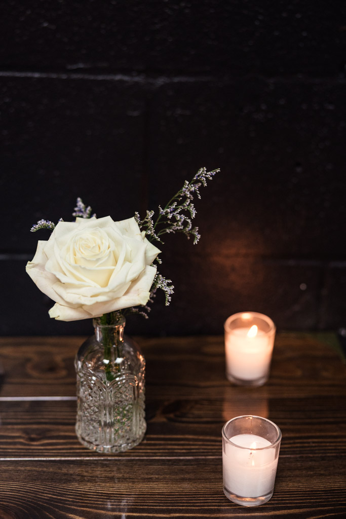 A white rose in a glass vase and two lit candles on a wooden table for Chicago Winery wedding reception
