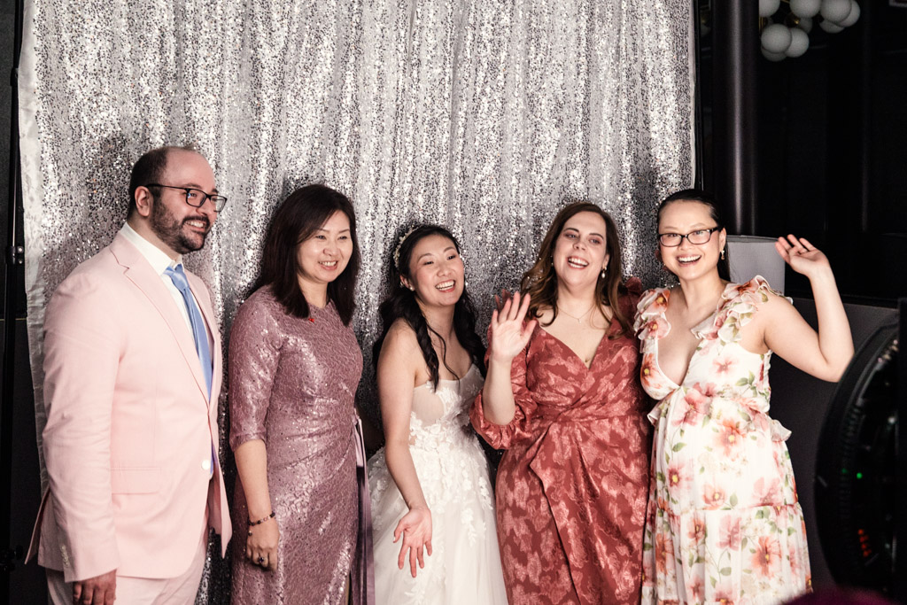 Bride and guests pose and smile in front of a sparkling silver backdrop while using the photo booth at a Chicago Winery wedding reception