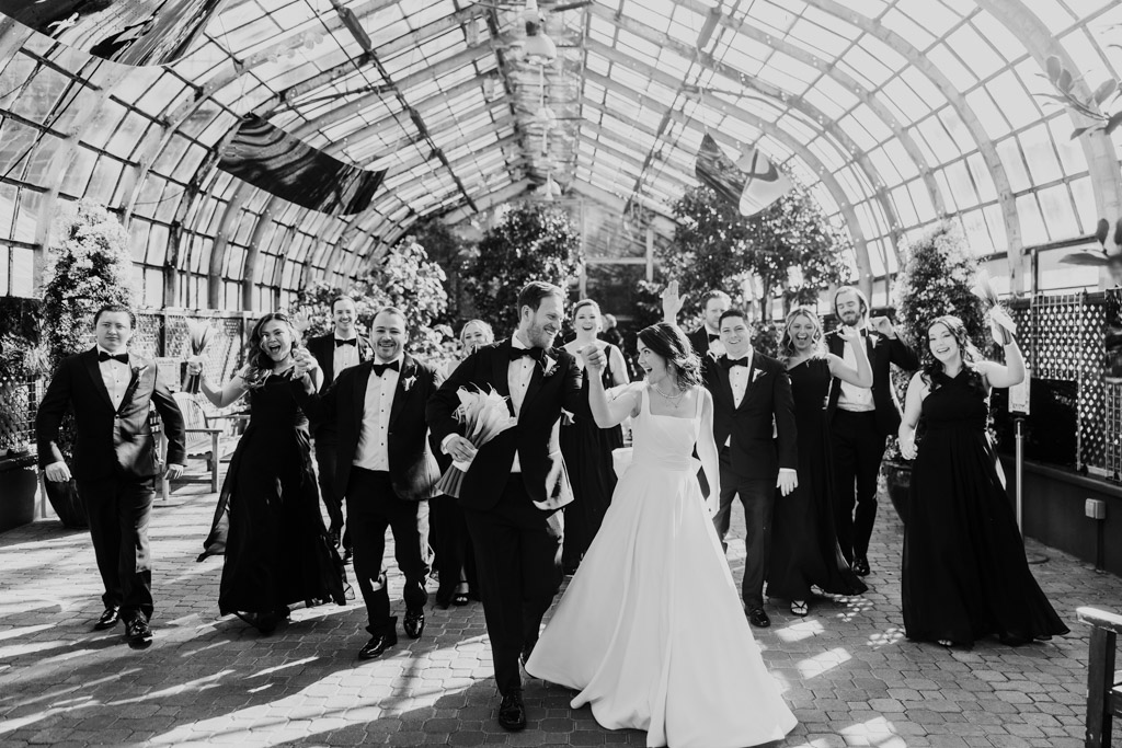 Black and white photo of wedding party walking through a greenhouse at Lincoln Park Conservatory