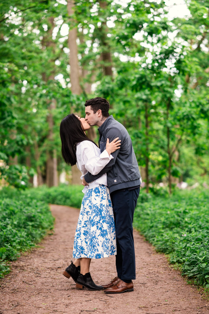 Engaged couple kisses on a tree-lined path in Oak Park's Austin Gardens