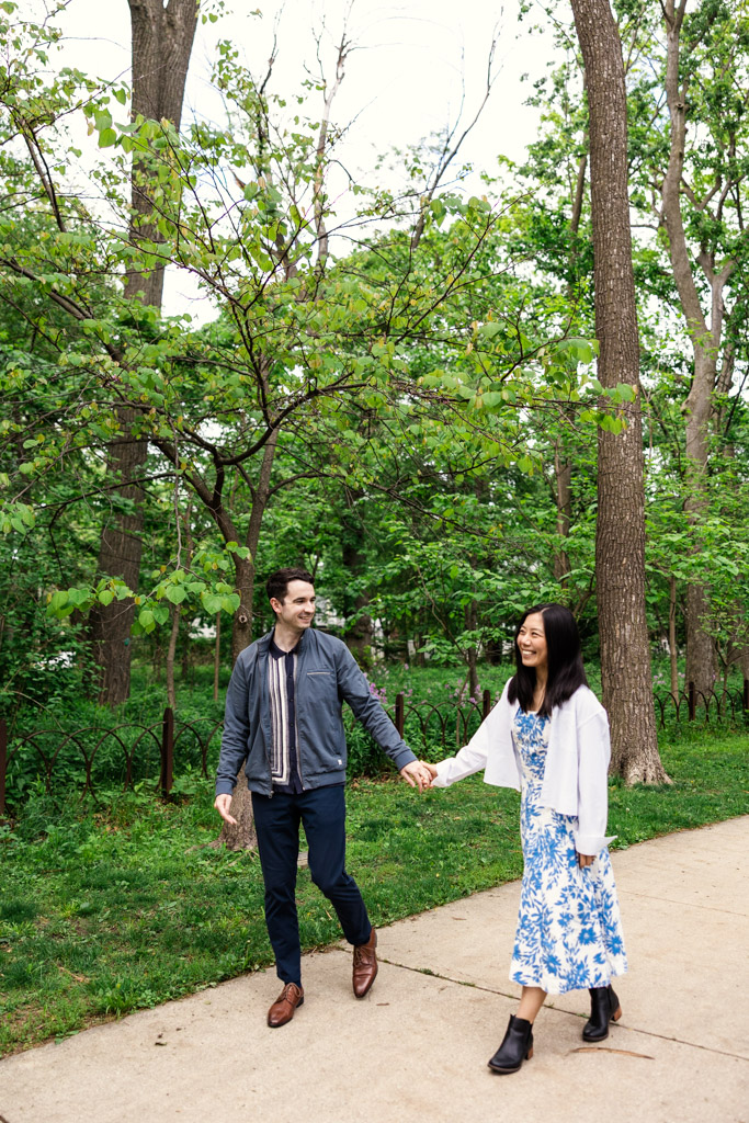A couple holding hands and smiling while walking on a path in Oak Park's Austin Gardens during their engagement session