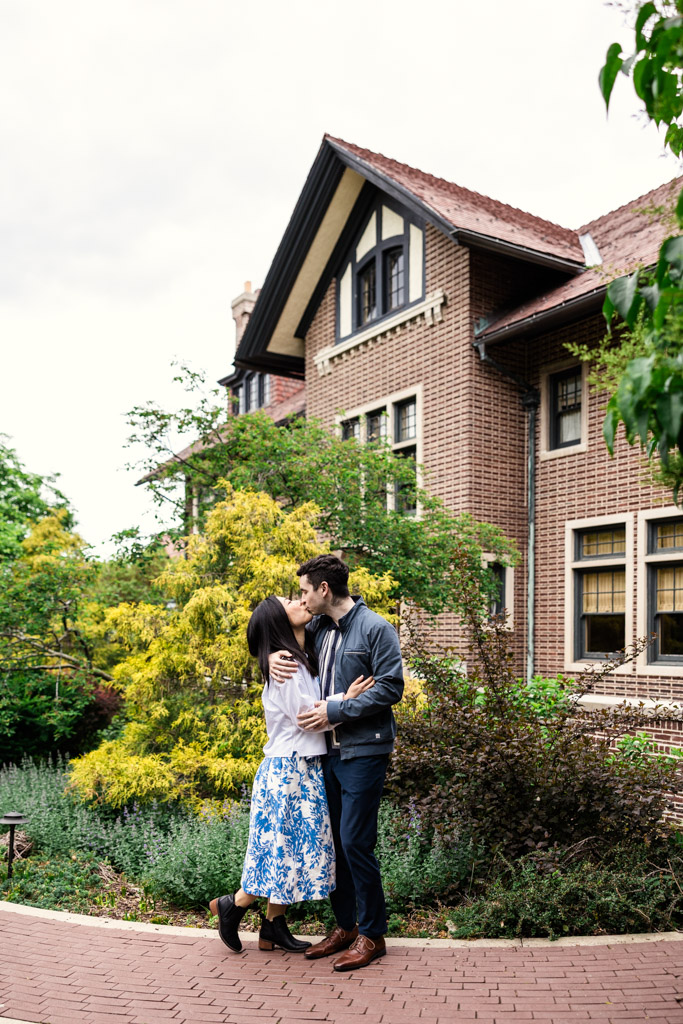 A couple kisses outside Cheney Mansion surrounded by greenery and trees during their Oak Park engagement session