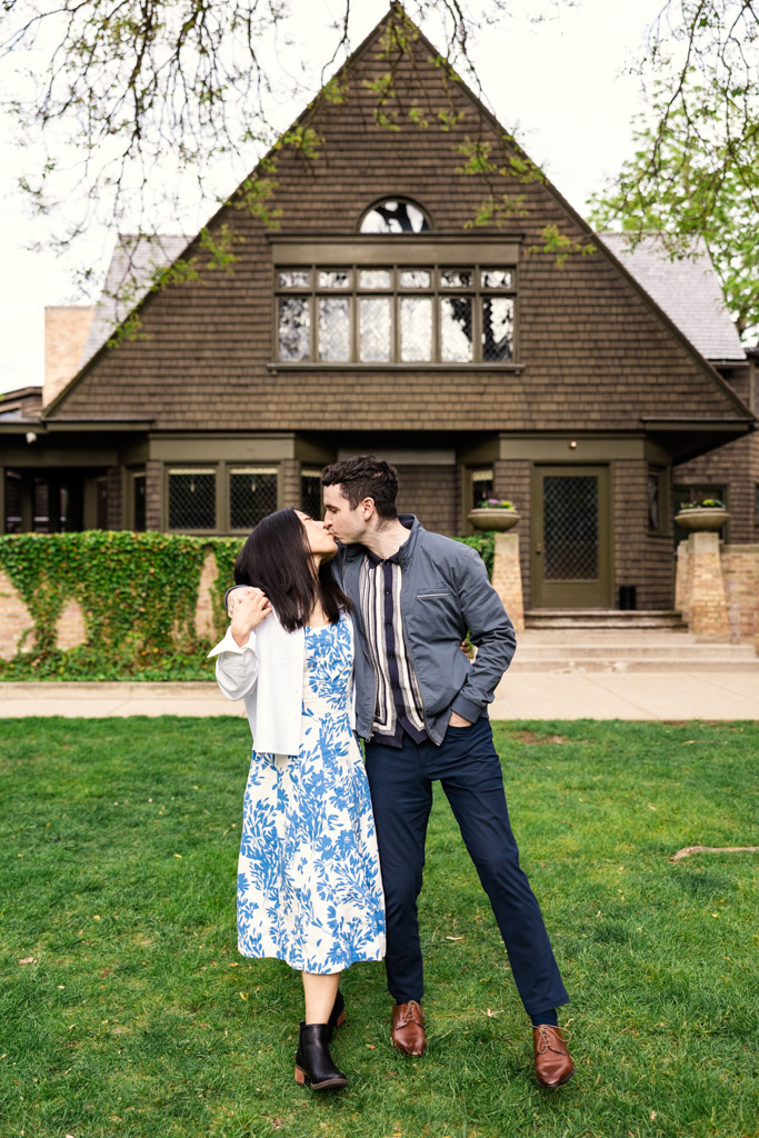 Couple kisses while standing on grass in front of the Frank Lloyd Wright Home and Studio during their Oak Park engagement session