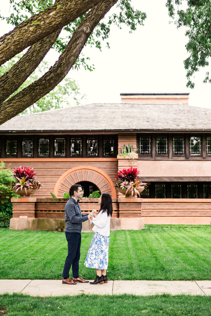 A couple stands facing each other on a lawn in front of the Frank Lloyd Wright Home and Studio during their Oak Park engagement session