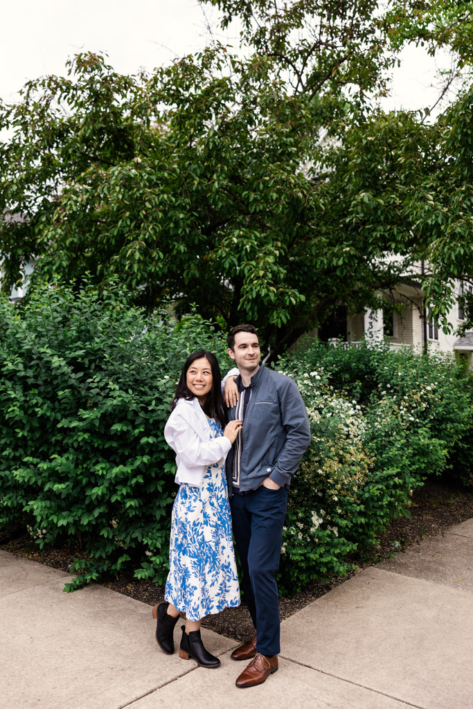 Portrait of engaged woman and man smiling outside in front of green leafy bushes and trees in Oak Park