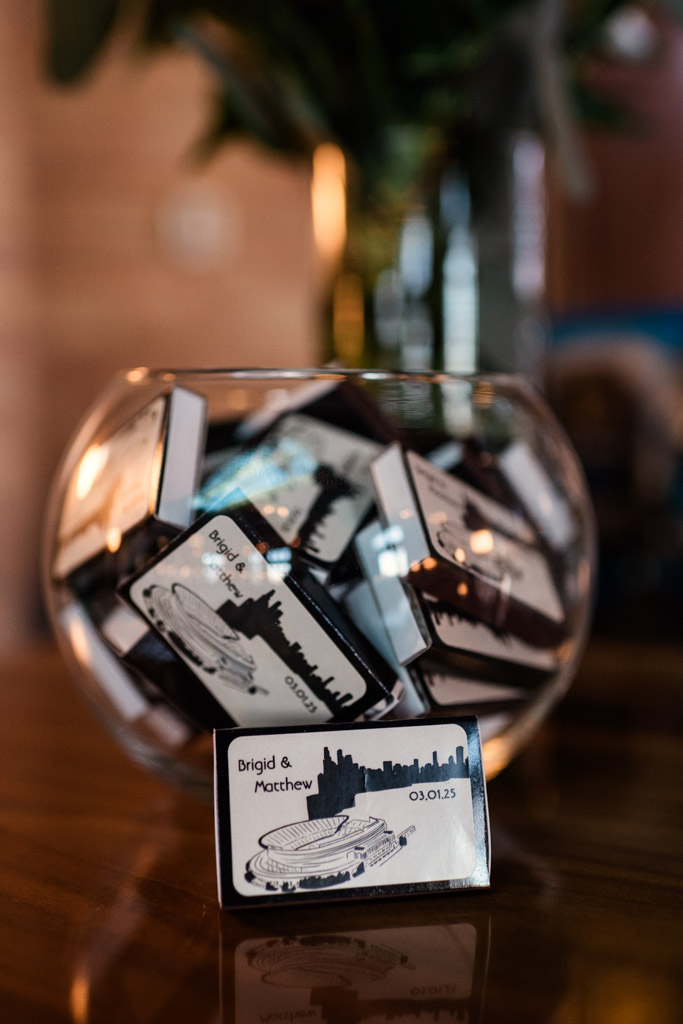 A glass bowl filled with custom Cafe Brauer wedding favor matchboxes; one matchbox is displayed in front