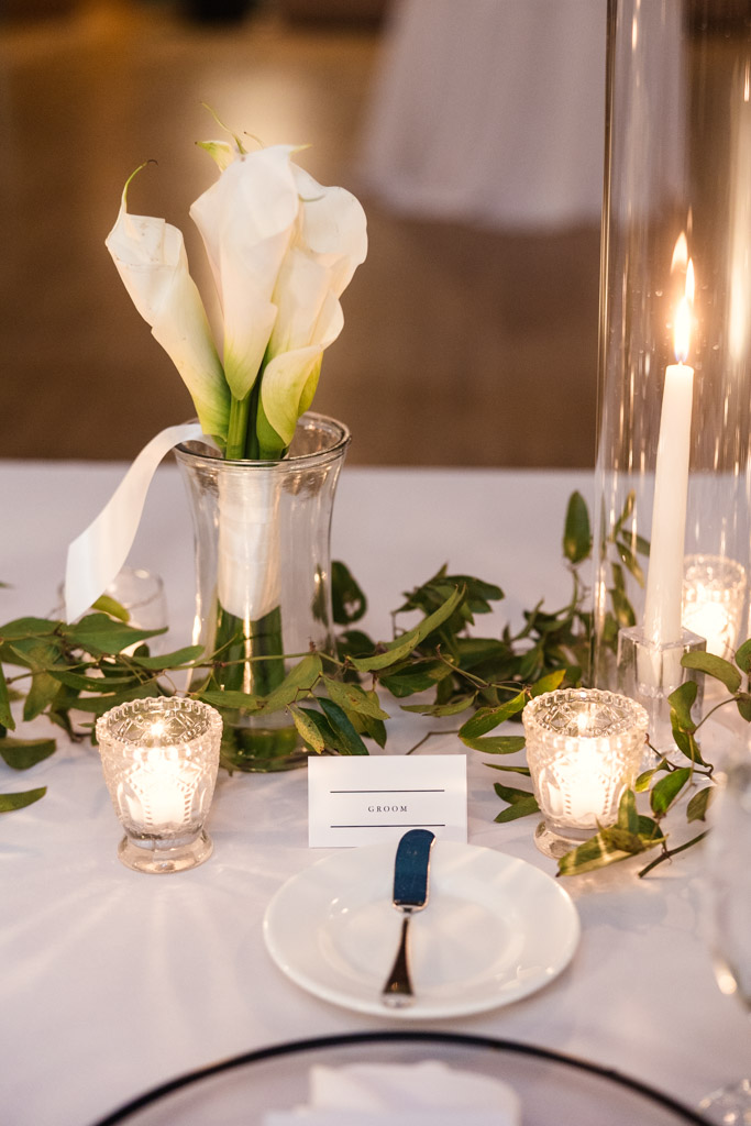 Groom's place setting for Cafe Brauer wedding reception features white calla lilies in a vase, candles and greenery