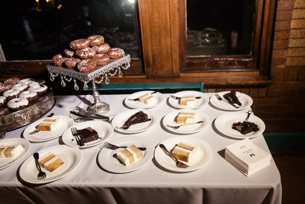 Dessert table with plates of cake slices, and trays of donuts for Cafe Brauer wedding reception