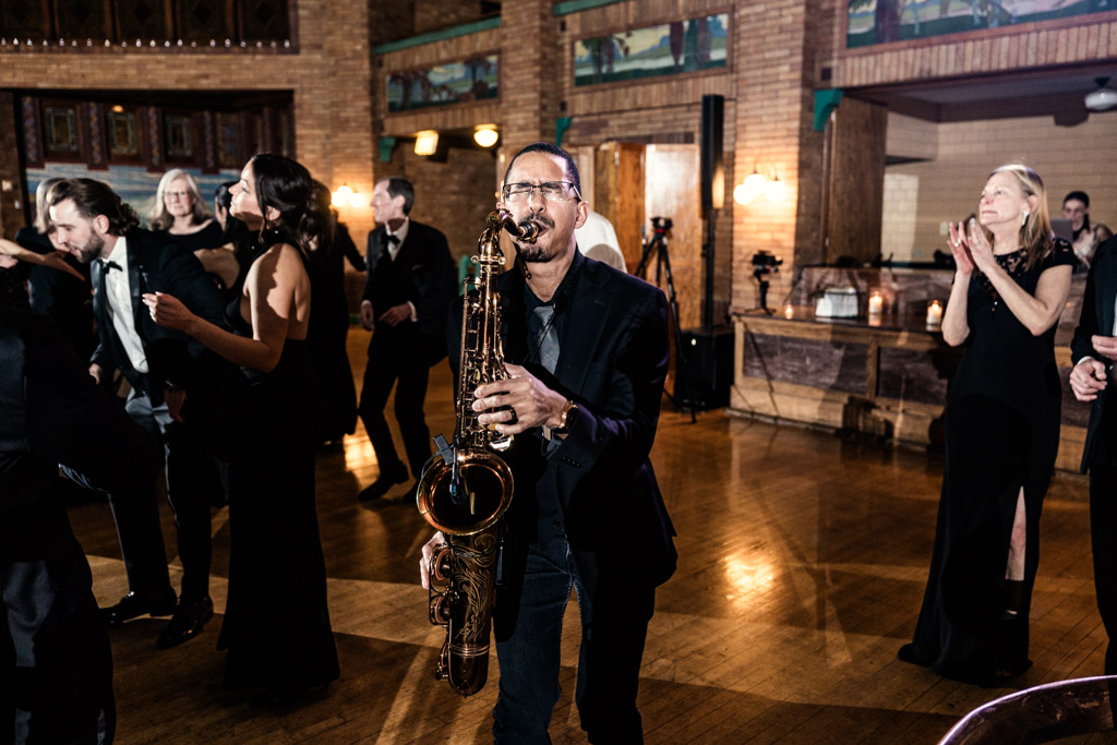 Derrick Tate plays saxophone on the Cafe Brauer dance floor while guests in formal wear dance and clap around him during spring wedding reception