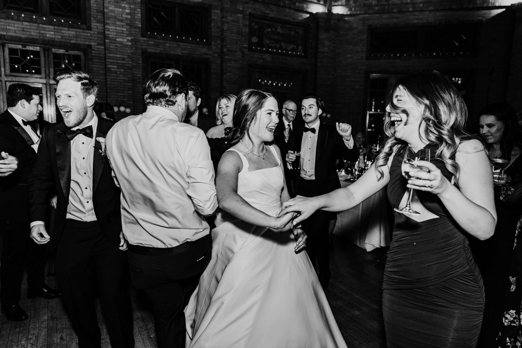 Black and white photo of bride, groom and guests laughing on the dance floor during their Cafe Brauer wedding reception