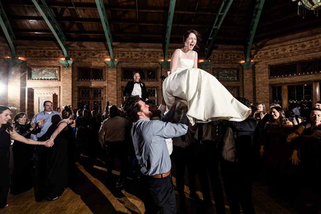 Guests lift the bride and groom in chairs as part of the hora during their wedding reception at Cafe Brauer.