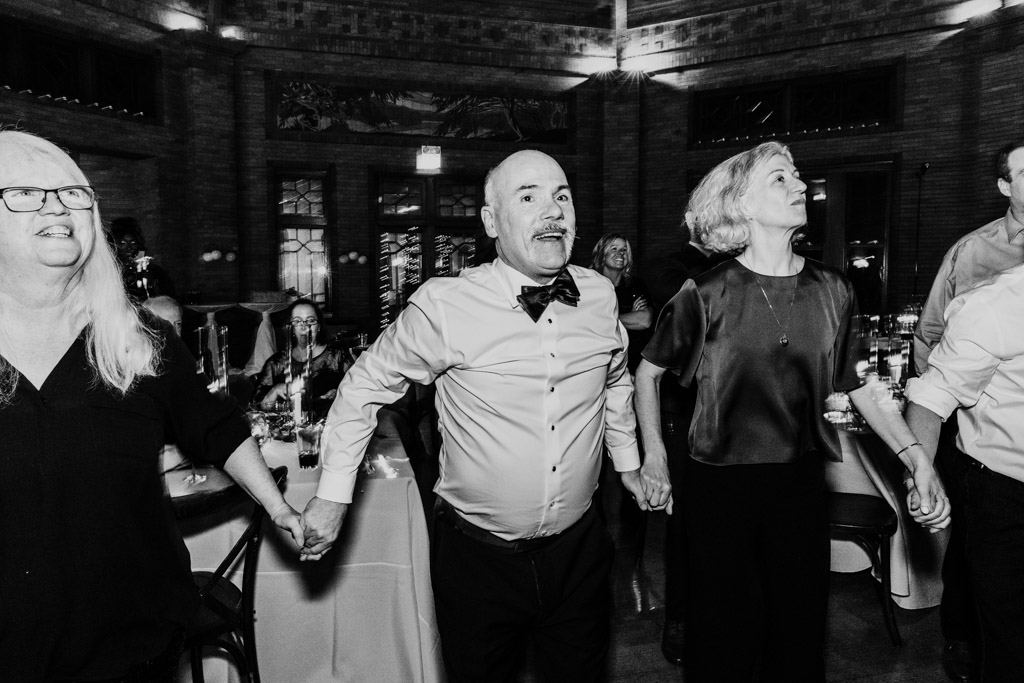 lack and white photo of guests holding hands and smiling on the dance floor during Cafe Brauer wedding reception