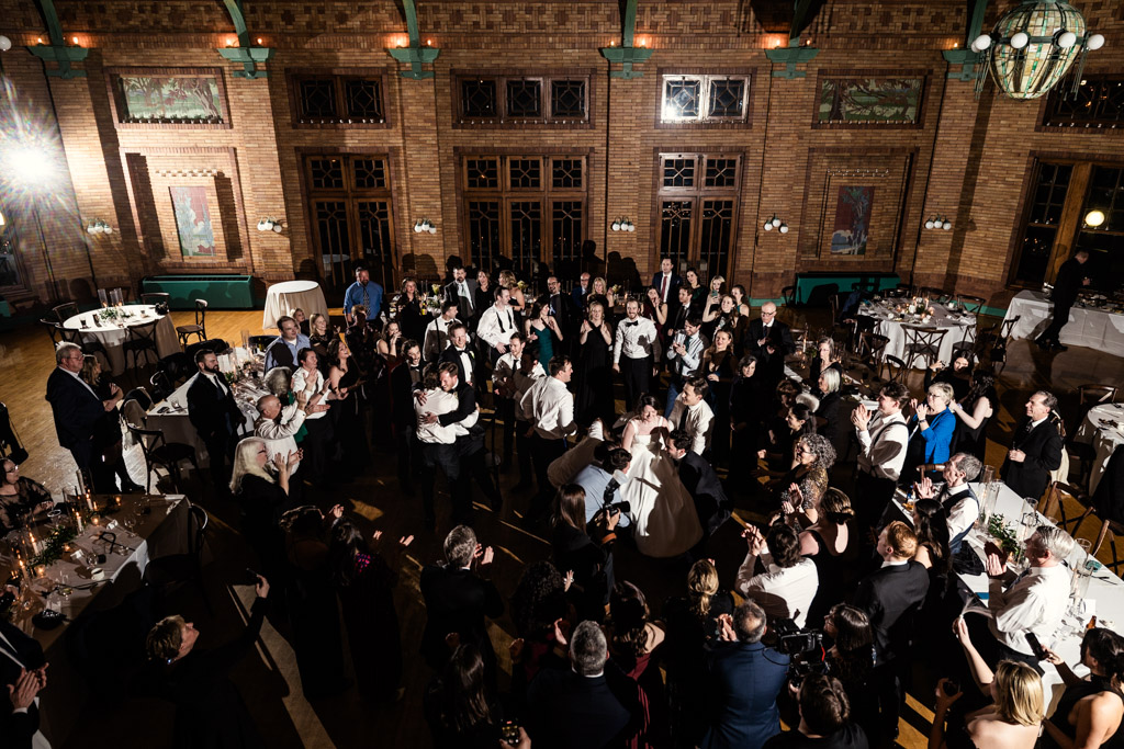 Bride and groom on the dance floor at Cafe Brauer, surrounded by cheering wedding guests as seen from the venue's balcony